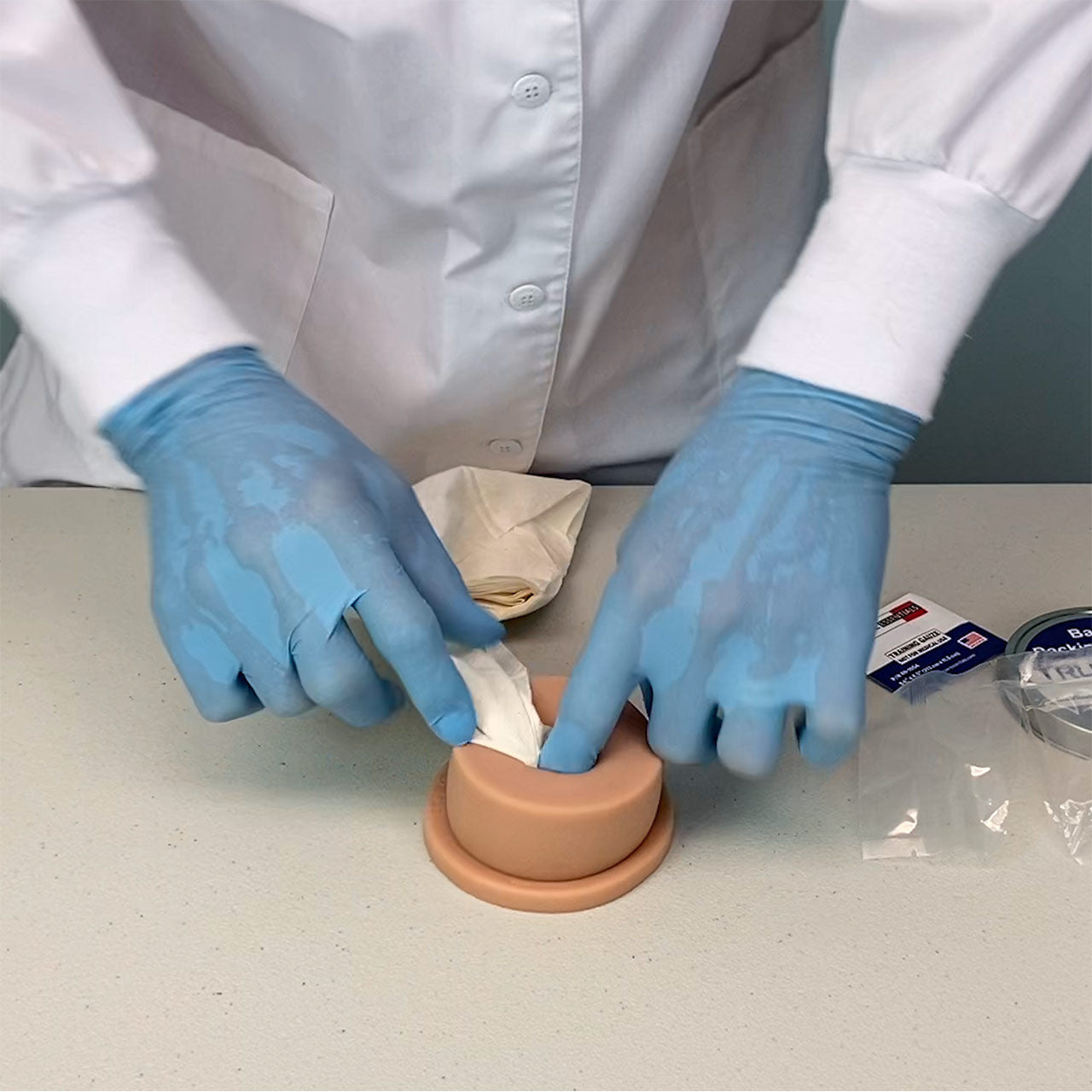Light Tone Luna TrueClot Basic Packing Trainer (BPT) example of someone in gloved hands packing the wound packing trainer